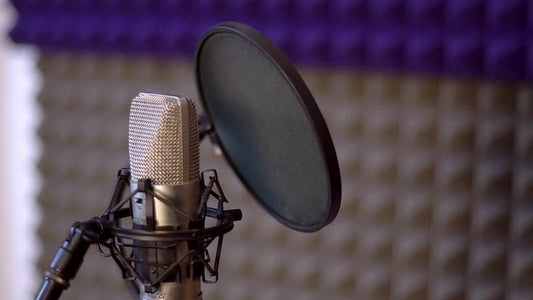 Studio condenser microphone with a pop filter positioned in front, set up for vocal recording against a sound-treated acoustic foam background.