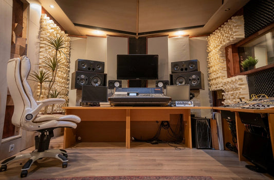 Professional recording studio control room featuring a large mixing console, studio monitors, acoustic treatment panels, and a central workstation designed for music production and audio mixing.