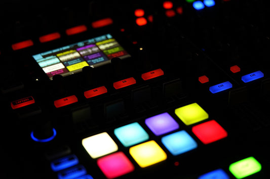 Close-up of a colorful music production controller with illuminated pads, knobs, and buttons in a dark studio setting