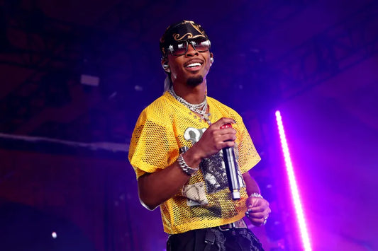 D4VD in a yellow mesh shirt and sunglasses holding a microphone on stage under purple lighting