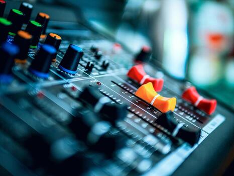 Close-up of an audio mixing console with colorful knobs and faders, including prominent red and orange sliders, used in music production.
