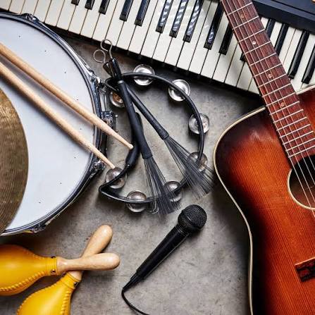 Musical instruments arranged together, including a keyboard, acoustic guitar, drum, tambourine, microphone, drumsticks, brushes, and maracas.