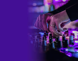 Hands adjusting knobs on an audio mixing console under purple stage lighting.