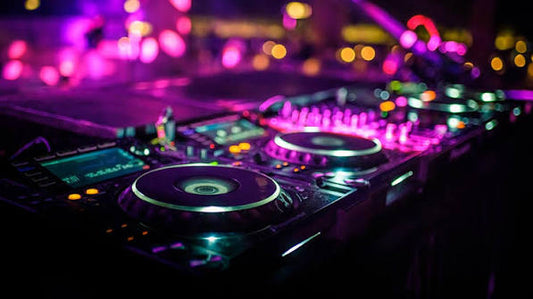 DJ turntables and mixing equipment illuminated by vibrant pink, purple, and green club lighting.