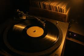 Vinyl record spinning on a turntable in warm lighting, with shelves of records visible in the background.