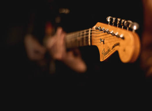 Close-up of an electric guitar headstock with the musician blurred in the background.