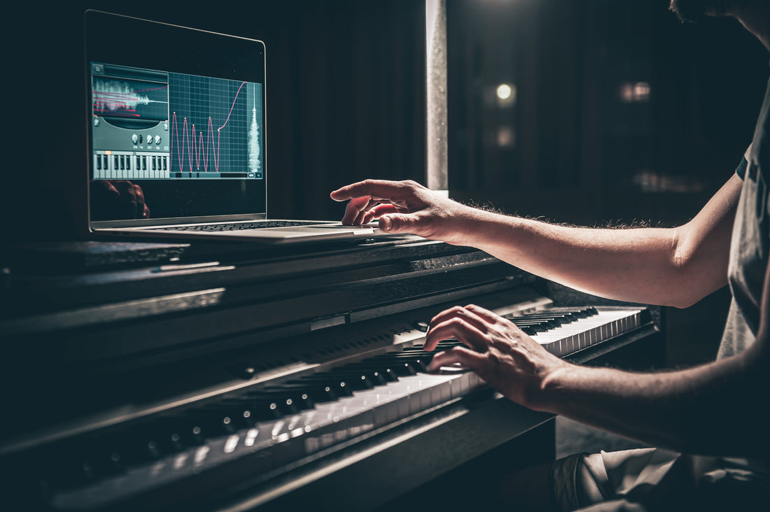 Producer using music production software on a laptop while playing a keyboard in a home recording studio.