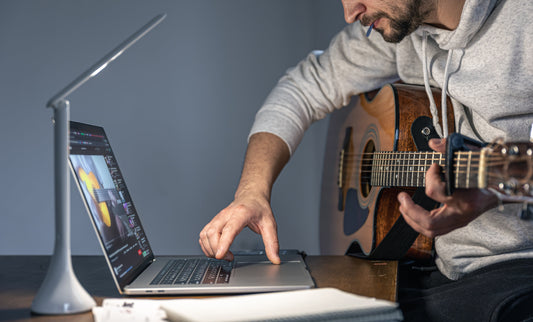 Musician learning guitar online using laptop and acoustic guitar.
