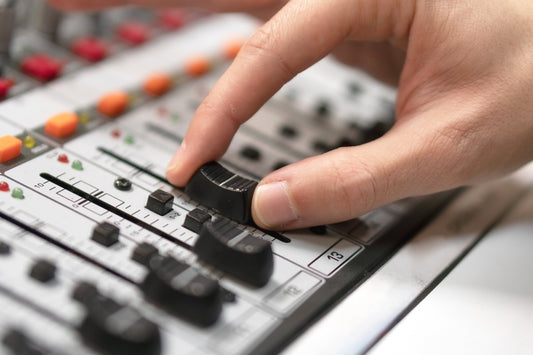Close-up of a hand adjusting a fader on a professional audio mixing console, surrounded by various knobs, buttons, and sliders.