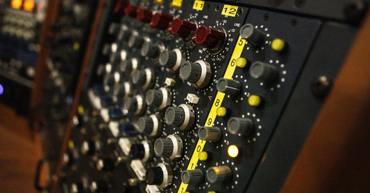 Close-up of a professional analog audio mixing console with multiple rotary knobs, gain controls, and numbered channel strips used in a recording studio.