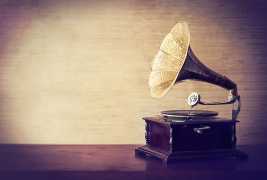 Vintage gramophone with a brass horn playing a vinyl record on a wooden table against a soft, neutral background.