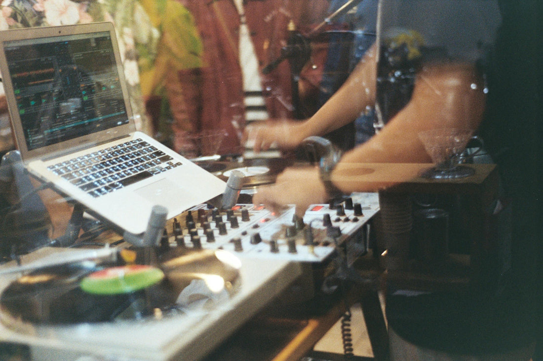 DJ performing live with a laptop, mixer, and turntables in a studio setting, adjusting controls during a music production session.