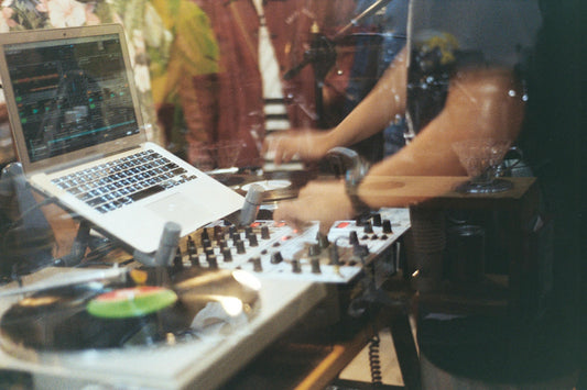 DJ performing live with a laptop, mixer, and turntables in a studio setting, adjusting controls during a music production session.