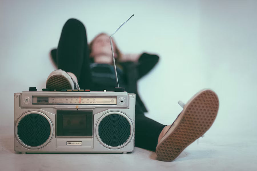 Retro boombox radio on the floor with a person relaxing behind it, feet up, creating a nostalgic music listening scene.