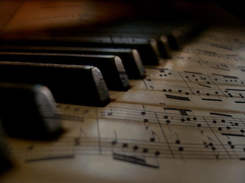 Close-up of piano keys resting over a sheet of printed music, with musical notes visible beneath the keyboard in warm, low lighting.