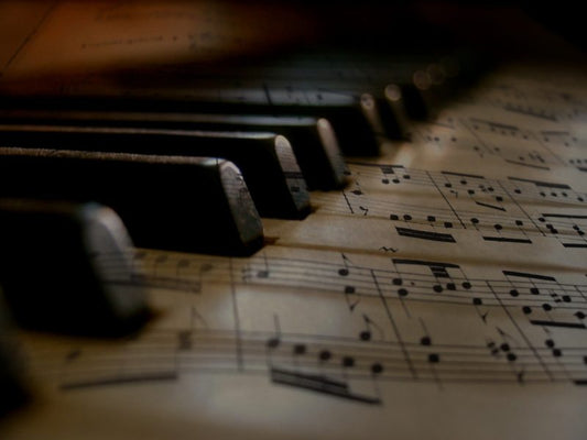 Close-up of piano keys resting over a sheet of printed music, with musical notes visible beneath the keyboard in warm, low lighting.