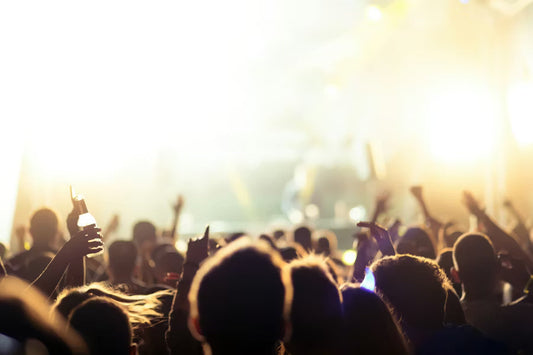 Crowd at a live concert with raised hands and glowing stage lights, capturing the energy of a music festival audience.