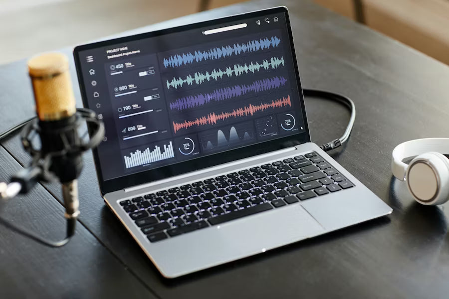 Home studio setup with a laptop displaying audio mixing software waveforms, a condenser microphone, and headphones on a desk.