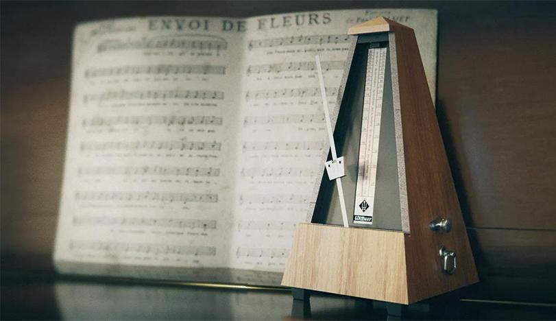 A wooden mechanical metronome placed on a piano, with sheet music open in the background.